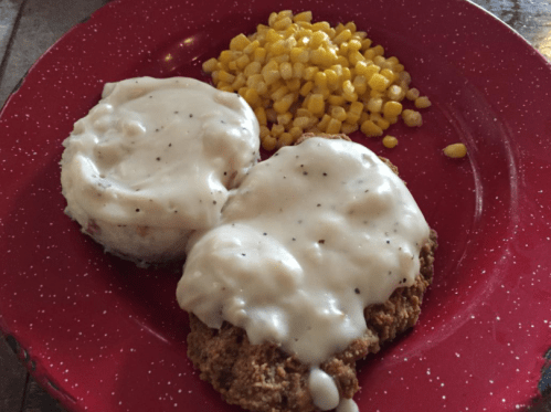 A red plate with two biscuits covered in white gravy and a side of yellow corn.