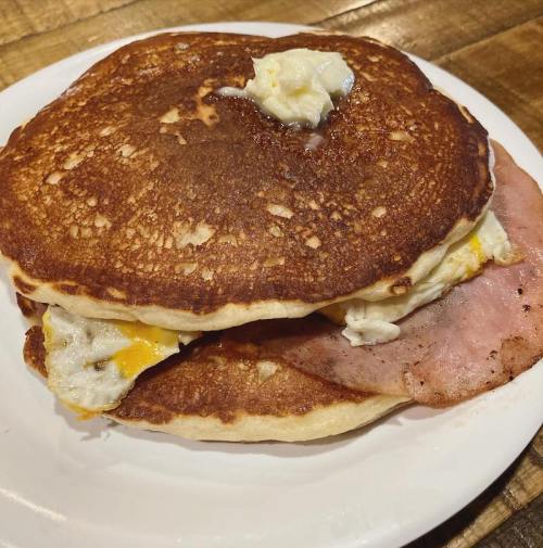 A plate with two fluffy pancakes, topped with butter, and filled with a fried egg and slices of ham.