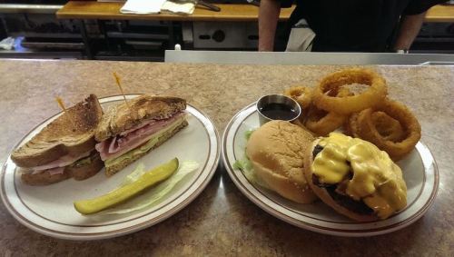 A plate with a sandwich, pickle, and onion rings next to a cheeseburger with melted cheese and lettuce.