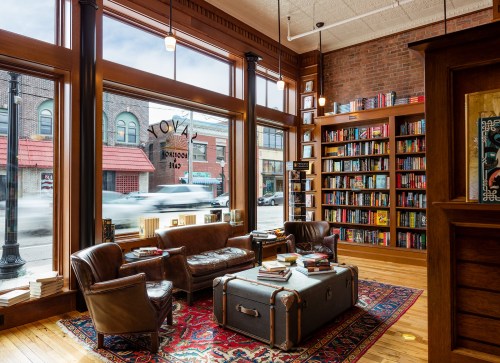 Cozy bookstore interior with leather chairs, a vintage trunk, and shelves filled with books, featuring large windows.