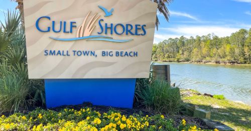 Sign for Gulf Shores in Alabama featuring the tagline 'Small Town, Big Beach,' surrounded by greenery and water.