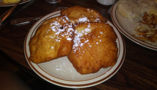 A plate of three golden-brown fried pastries dusted with powdered sugar.
