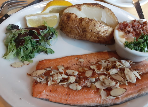 A plate featuring baked salmon topped with almonds, a baked potato, lemon wedges, and a side salad.