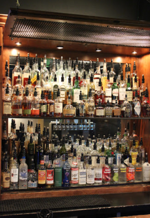 A well-stocked bar featuring a variety of liquor bottles on wooden shelves, illuminated by soft lighting.