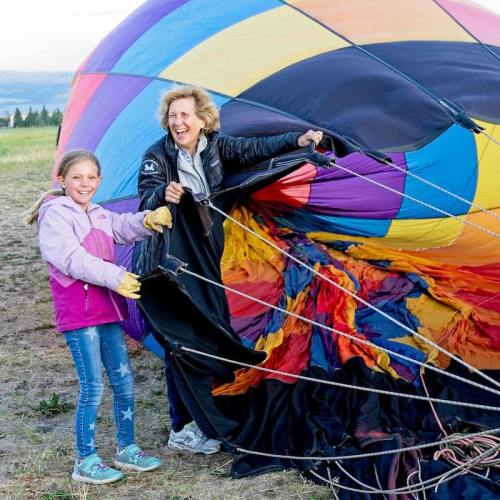A woman and a girl joyfully hold the fabric of a colorful hot air balloon on a grassy field.