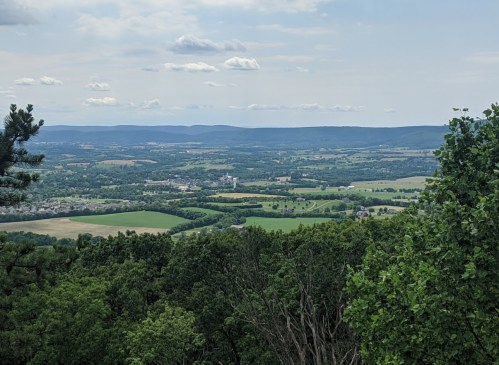 A panoramic view of lush green fields and rolling hills under a partly cloudy sky.