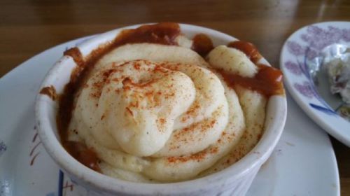 A bowl of creamy mashed potatoes topped with a drizzle of sauce and a sprinkle of paprika.