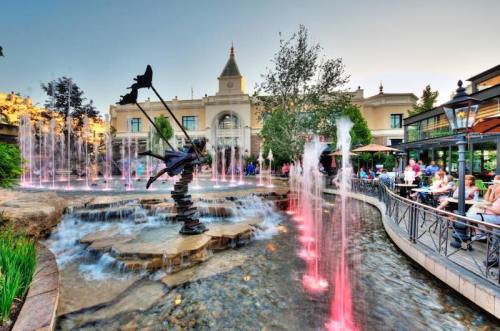 A scenic view of a fountain with colorful lights, a statue, and a restaurant patio in the background.