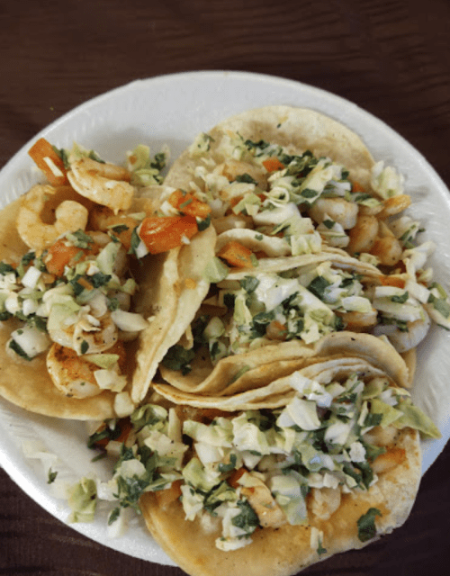A plate of shrimp tacos topped with cabbage, tomatoes, and cilantro on corn tortillas.