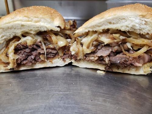Close-up of a sliced sandwich filled with tender beef, caramelized onions, and melted cheese on a sesame seed bun.