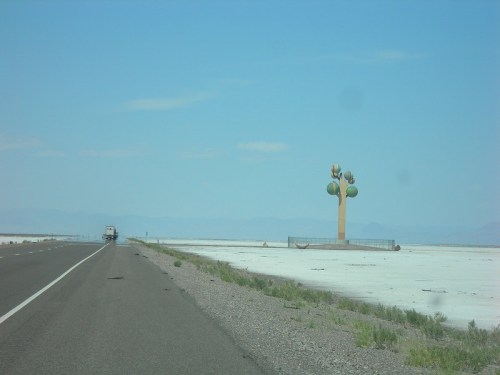 A large, colorful cactus sculpture stands beside a highway in a flat, arid landscape under a clear blue sky.