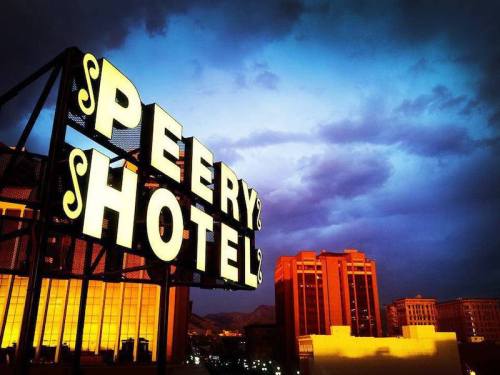 Sign of Peery Hotel illuminated against a dramatic twilight sky with clouds and city buildings in the background.