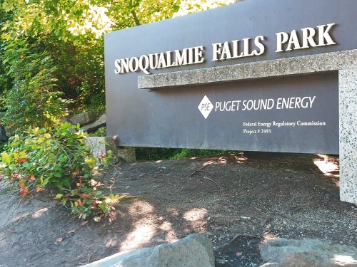 Sign for Snoqualmie Falls Park, featuring the Puget Sound Energy logo and surrounded by greenery.