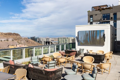 Rooftop terrace with modern seating, overlooking a cityscape and mountains under a partly cloudy sky.