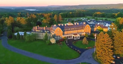 Aerial view of a large stone hotel surrounded by lush greenery and rolling hills at sunset.