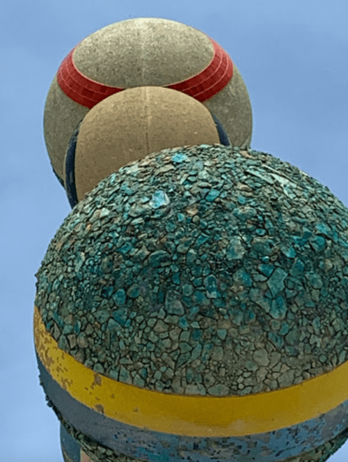 Three colorful spheres stacked vertically, featuring textured surfaces and varying patterns against a blue sky.