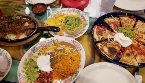 A table spread with sizzling fajitas, quesadillas, rice, beans, guacamole, salsa, and tortilla chips.
