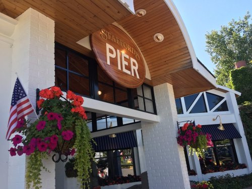 Exterior of Stafford's Pier restaurant, featuring a large sign and colorful flower baskets, with an American flag nearby.