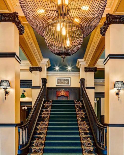 Elegant staircase with a green carpet, ornate chandelier, and decorative wall sconces in a stylish interior.