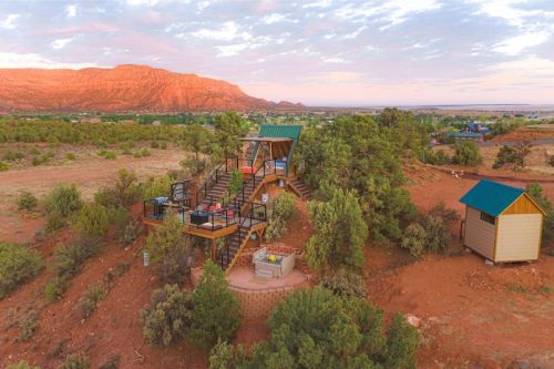 Aerial view of a modern cabin surrounded by desert landscape and mountains at sunset.
