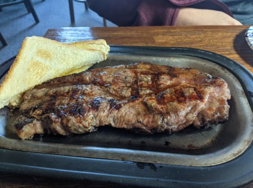 A grilled steak on a sizzling plate, accompanied by a slice of toasted bread.