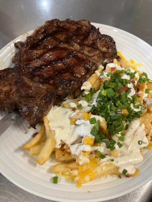 A plate of grilled steak next to loaded fries topped with cheese, sour cream, and chopped green onions.