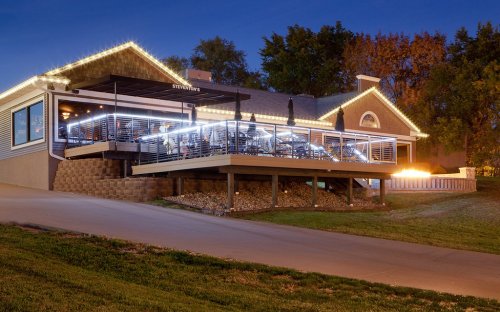 A restaurant exterior at dusk, featuring outdoor seating with lights and a welcoming atmosphere.