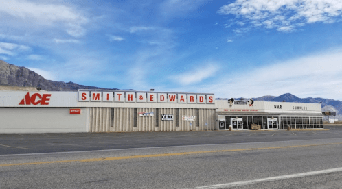 A storefront featuring "Smith & Edwards" and "ACE" signs, with mountains and a blue sky in the background.