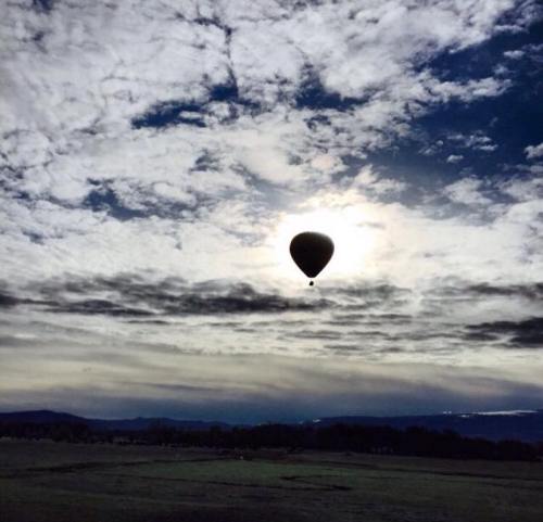 A hot air balloon floats against a backdrop of cloudy skies and a glowing sun.