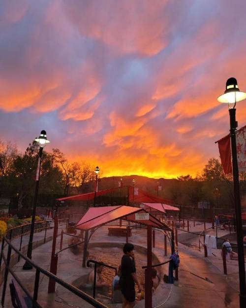 A vibrant sunset with orange and purple clouds over a park, featuring lampposts and a playground area.