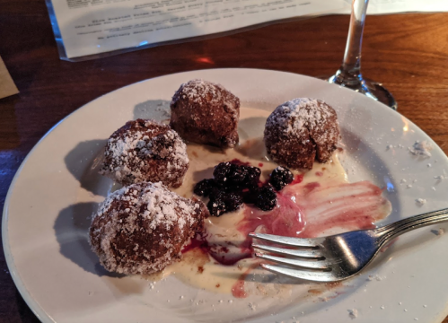 Four chocolate dessert balls dusted with powdered sugar on a plate with berry sauce and a fork.