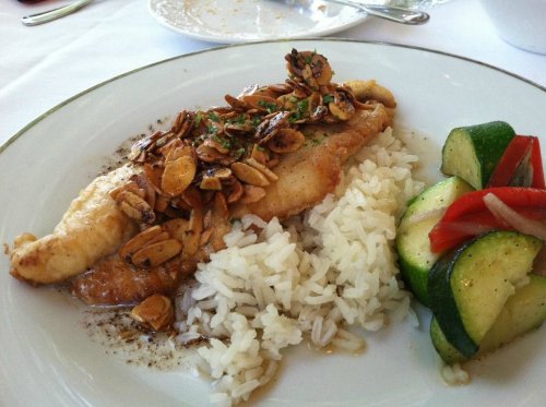 A plate of fish topped with almonds, served with rice and sautéed zucchini and bell peppers.