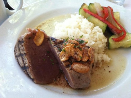 A plate featuring grilled tuna steak topped with garlic, served with rice and sautéed vegetables.