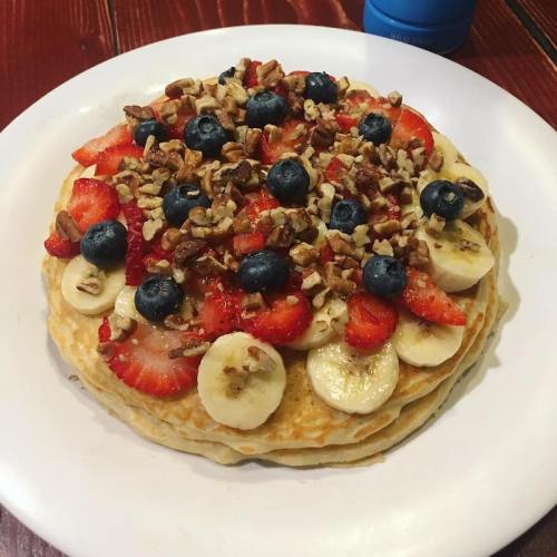 A stack of pancakes topped with sliced bananas, strawberries, blueberries, and chopped nuts on a white plate.