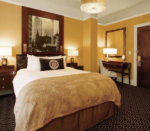 Cozy hotel room with a queen bed, warm yellow walls, a desk, and a large mirror, featuring elegant decor.