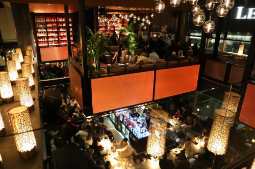 A bustling restaurant interior with multiple levels, dim lighting, and a vibrant bar area filled with patrons.