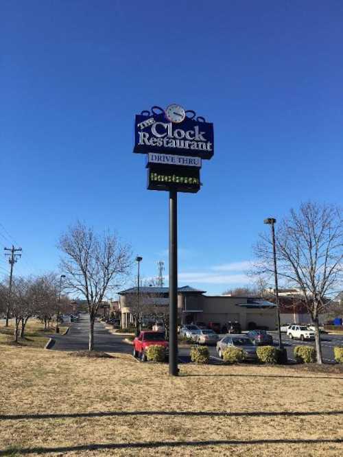 Sign for The Clock Restaurant with a drive-thru, set against a clear blue sky and a parking lot.