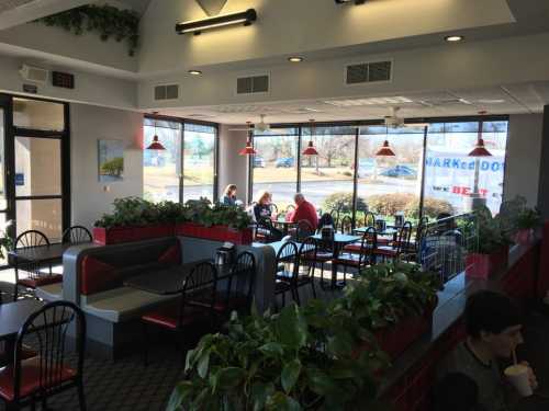 A bright restaurant interior with plants, tables, and customers enjoying their meals by large windows.