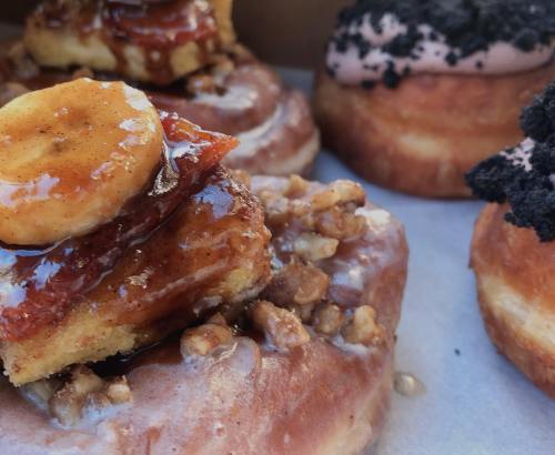 A close-up of assorted donuts, featuring a glazed donut topped with caramelized bananas and nuts, and a chocolate-frosted donut.