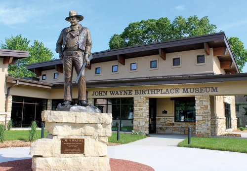 Statue of John Wayne in front of the John Wayne Birthplace Museum, featuring a modern building and landscaped grounds.