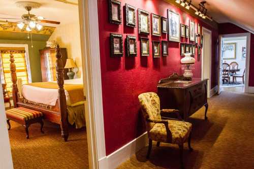 A cozy hallway with red walls, framed photos, a vintage chair, and a glimpse of a bedroom in the background.