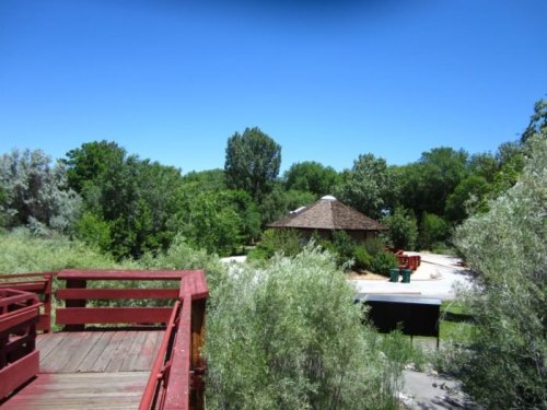 A wooden deck overlooks a lush green area with a round building and picnic tables under a clear blue sky.