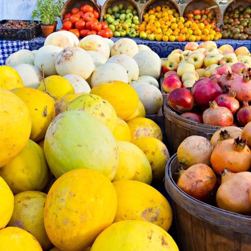A vibrant market display featuring various melons, apples, and pomegranates in wooden baskets and on a table.
