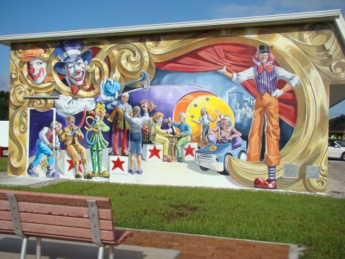 Colorful mural depicting clowns and circus performers in a vibrant, playful scene with a backdrop of curtains and stars.
