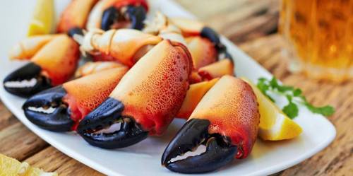 A plate of vibrant crab claws with a side of lemon wedges, set on a rustic wooden table.