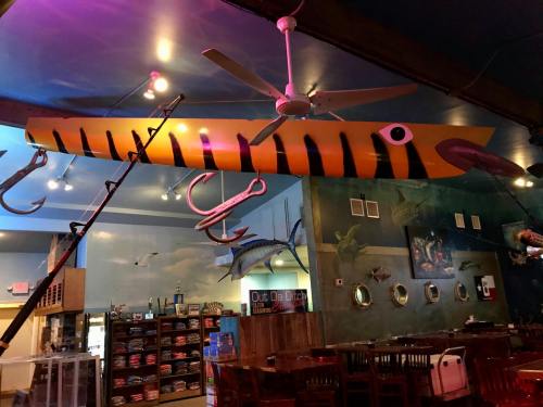 A colorful, oversized squid model hangs from the ceiling of a seafood restaurant, with fishing gear and decor in the background.