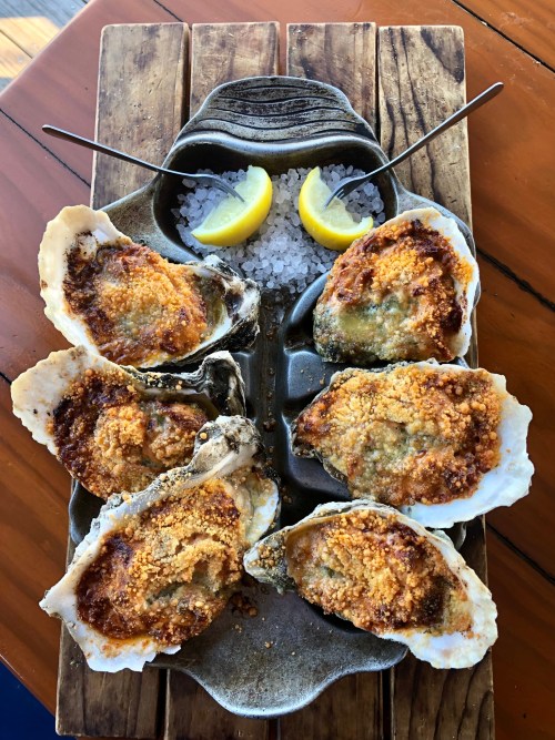 A platter of baked oysters topped with breadcrumbs, served with lemon wedges and sea salt.