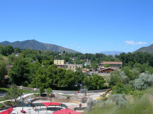 A scenic view of a small town surrounded by green trees and mountains under a clear blue sky.