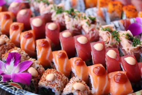 A colorful assortment of sushi rolls and sashimi, garnished with flowers and sauces, arranged on a platter.