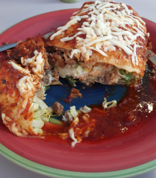 A colorful plate featuring a large, stuffed burrito topped with cheese and sauce, with a portion cut out.